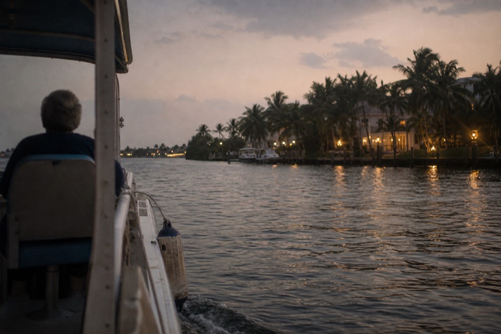 A riverboat moving along the New River at dusk past lit waterfront homes, no text, no logos, no people