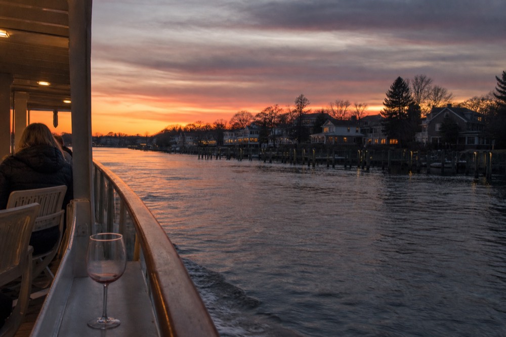 A riverboat with warm lights cruising past waterfront homes at dusk, no text, no logos, no people.