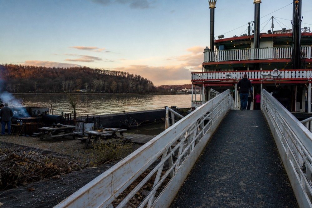 Riverboat at a dock in evening light with a barbecue dinner setting visible on shore, no text, no logos, no people.